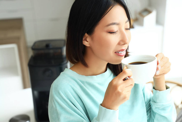 Belle femme asiatique avec tasse de café chaud dans la cuisine, gros plan - Photo, image