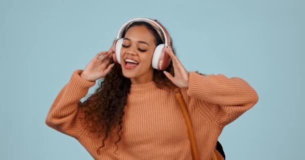Headphones, dancing and happy woman student with music, radio and isolated in a studio blue background. Happiness, joy and young person streaming audio for energy movement and celebration with smile. - Footage, Video