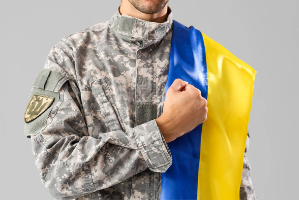 灰色の背景にウクライナの旗を持つ男性兵士 - 写真・画像
