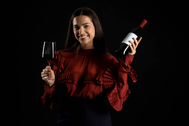 Siyah arka planda cam ve şarap şişesi olan genç bir kadın. - Fotoğraf, Görsel