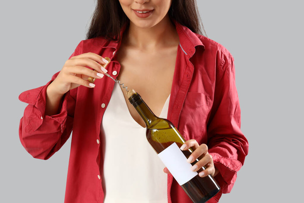 Belle jeune femme asiatique avec bouteille de vin et tire-bouchon sur fond gris - Photo, image