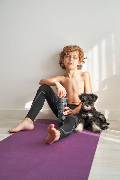 Koko kehon paljain jaloin poika istuu matto pieni koira ja katselee kameraa, kun ottaa tauko harjoitus - Valokuva, kuva