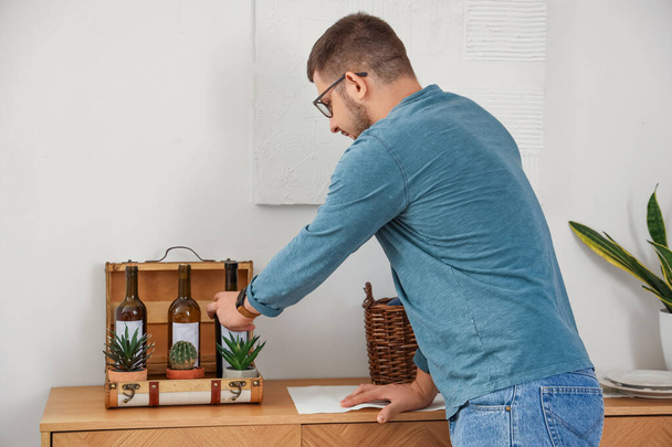 Junger Sommelier holt Flasche Wein aus Koffer in der heimischen Küche - Foto, Bild