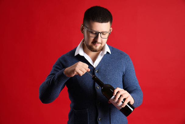 Junger Sommelier öffnet Flasche Wein mit Korkenzieher auf rotem Hintergrund - Foto, Bild