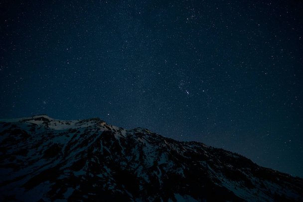 Dal basso catena montuosa mozzafiato coperta di neve contro il buio cielo stellato di notte in campagna - Foto, immagini
