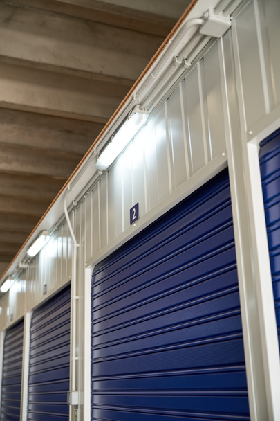 From below of numbered storage items with blue metal roller doors and bright lamps in modern storehouse - Photo, Image