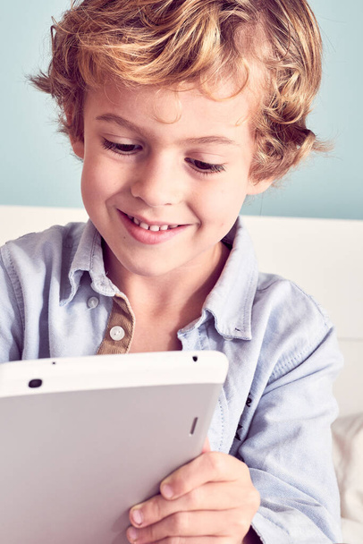 Crop suloinen positiivinen poika kihara hiukset selailu moderni tabletti ja hymyillen kirkkaasti - Valokuva, kuva