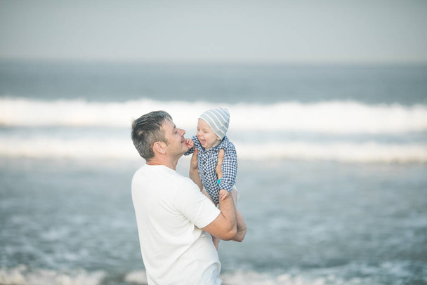Wesoły młody ojciec ze swoim synkiem bawią się razem nad morzem, tata wymiotuje dzieciakiem w powietrze - Zdjęcie, obraz