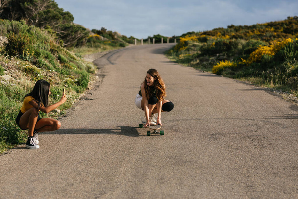 Tanımlanamayan etnik bir kadın, asfalt yolda uzun tahta otururken akıllı telefonunda geziniyor.  - Fotoğraf, Görsel