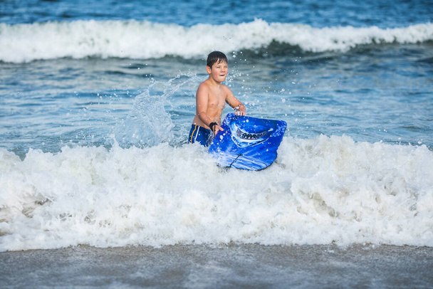 陽気な10代の少年が水泳ボードを持っている. ハッピーヨーロッパの家族は暑い夏の日に海に浮かぶ楽しさを持っています - 写真・画像
