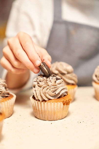 Nimetön kasvoton kokki saattaa evästeen suklaa täytteet maukkaita kotitekoisia cupcake valikoivasti keskittyä valoisa pöytä - Valokuva, kuva