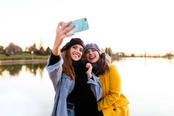 Casual γυναίκες που παίρνουν selfie στο smartphone στην ηλιόλουστη λίμνη - Φωτογραφία, εικόνα
