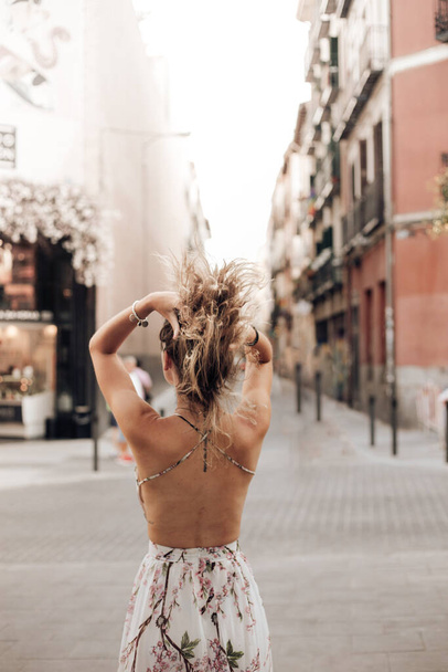Vue arrière de la jeune touriste tenant les cheveux tout en marchant sur la rue vide en plein jour - Photo, image