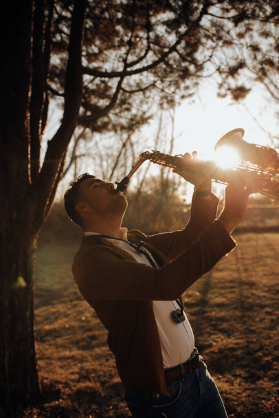 Genç müzisyen gün batımında saksafon çalıyor. - Fotoğraf, Görsel