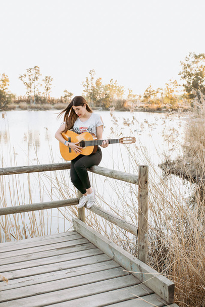 水の近くでギターを弾く若い女性 - 写真・画像