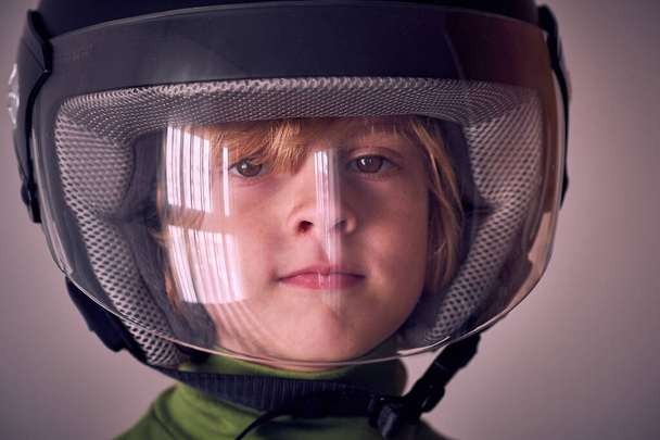 Portrait of cute little kid with blond hair and brown eyes wearing protective helmet with transparent plastic front and looking at camera - Photo, Image