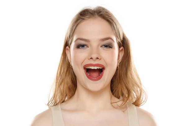 Portret van jonge gelukkig blonde vrouw met open mond op witte studio achtergrond - Foto, afbeelding