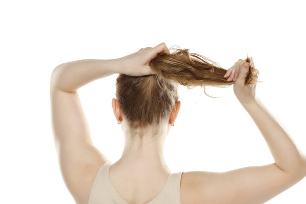 Сзади, вид сзади на молодую блондинку, завязывающую длинные волосы на белом фоне студии - Фото, изображение