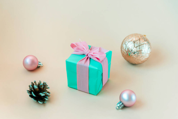 Teal modrá dárková krabice s růžovou mašlí, vánoční koule a borovice kužele na béžovém pozadí. - Fotografie, Obrázek