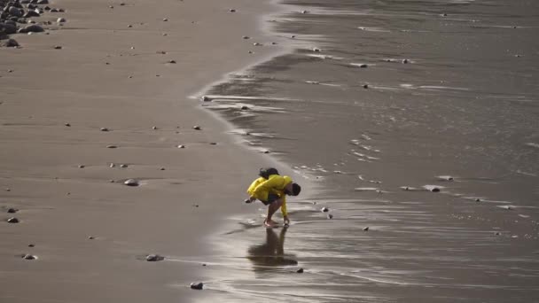 Madeira, Portugali - 2023.04.04 - 09: Mies, jolla on keltainen sadetakki kävelemässä pitkin Praia da Maiata rantaa, joka tunnetaan erinomaisista aalloistaan - Materiaali, video
