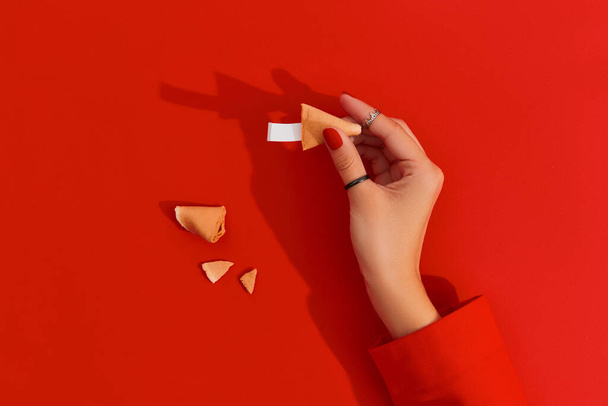 Kobiece ręce z manicure trzymające ciasteczko z wróżbą na czerwonym tle. Czysty papier do przewidywania słów. Makieta tła dla restauracji social media - Zdjęcie, obraz