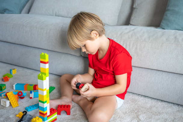 Aranyos kisfiú játszik színes játékok a padlón otthon - Fotó, kép