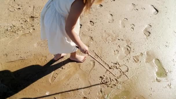 Menina criança desenho com um pau na areia na praia e se divertindo. Imagens 4k de alta qualidade - Filmagem, Vídeo
