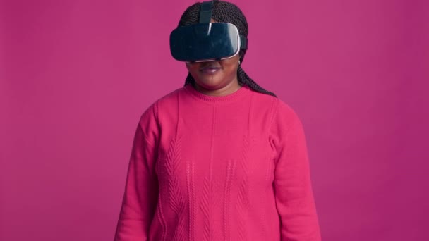 Інноваційна молода чорна жінка насолоджується футуристичним моделюванням з інтерактивним пристроєм, одягненим у 3D окуляри віртуальної реальності в студії. афроамериканська модниця використовує сучасну гарнітуру VR. - Кадри, відео