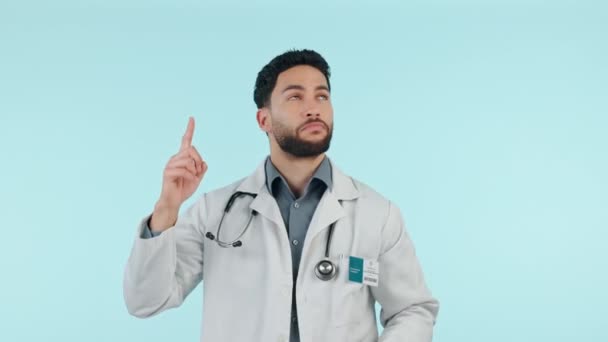 Doctor, man and pointing up for healthcare presentation, clinic news and happy information in studio. Face of medical professional marketing, choice and steps, guide or advice on a blue background. - Footage, Video