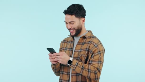 Happy man, phone and typing for social media, college communication and funny internet meme on blue background. Young person or student reading on mobile app for chat, news and laughing in studio. - Footage, Video