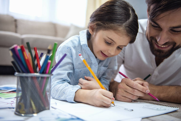 Cute little girl and her handsome father are drawing and smiling while playing together at home - Photo, Image
