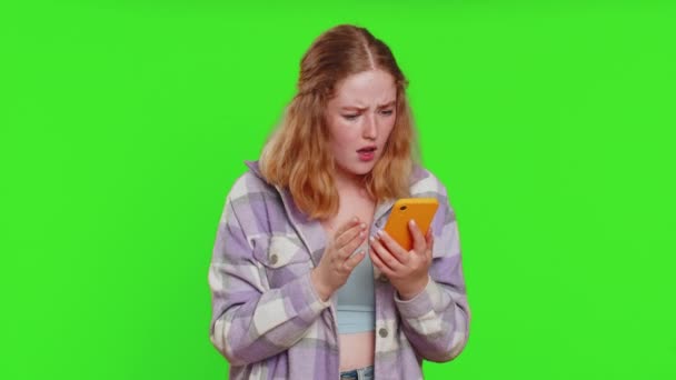 Upset sad woman use smartphone typing browsing, play game, loses, surprised by sudden lottery results bad fortune loss fail unlucky news. Sad redhead girl isolated on chroma key background, indoors - Footage, Video
