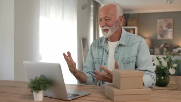 Ένας ηλικιωμένος συνταξιούχος παππούς με γκρίζα μαλλιά και γενειάδα λαμβάνουν δώρα σε κουτί ανοιχτή ανάγνωση κάρτα χαρούμενο χαμόγελο μπροστά από φορητό υπολογιστή στο σπίτι έχοντας online video call copy space - Πλάνα, βίντεο