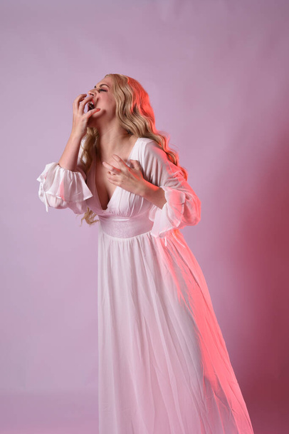 Close-up portret van mooie blonde model dragen elegante witte Halloween jurk. armen reiken uit als hongerige vampier. geïsoleerd op studio achtergrond met rode filmische stemmige verlichting. - Foto, afbeelding