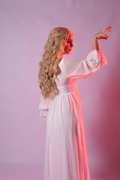 Primer plano retrato de la hermosa modelo rubia con elegante vestido de halloween blanco. brazos extendiéndose como vampiros hambrientos. aislado en el fondo del estudio con iluminación cinemática moody rojo. - Foto, Imagen
