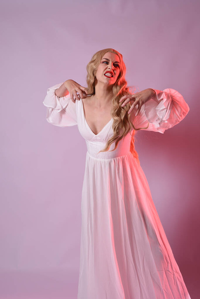 Крупним планом портрет красивої блондинки в елегантній білій сукні на Хеллоуїн. руки, що виходять, як голодний вампір. ізольовані на студійному фоні з червоним кінематографічним приглушеним освітленням. - Фото, зображення