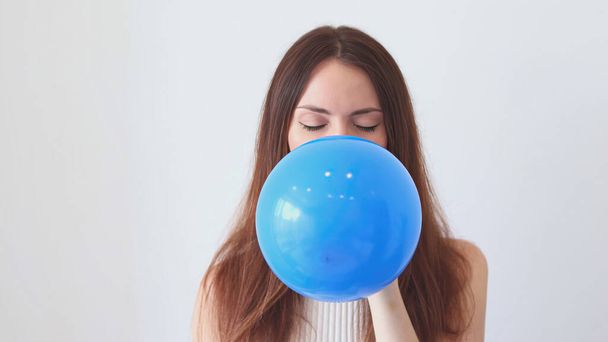 Μια όμορφη γυναίκα φουσκώνει ένα μπλε μπαλόνι - Φωτογραφία, εικόνα