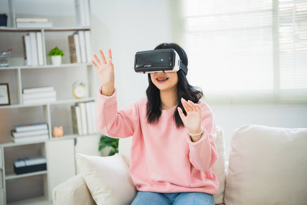 Aziatische vrouw glimlachen en VR spel te spelen, 3D divice nieuwe innovatie bril voor vermaak in de woonkamer thuis, aziatische vrouw blij in huis op vakantie. Gelukkig vrouw spelen metaverse VR technologie concept. - Foto, afbeelding