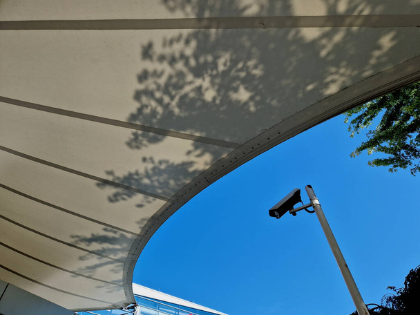 weiße Plane gespannt, Schatten vor Sonne und Regen über der Terrasse des Restaurants, auf dem Spielplatz im Kindergarten, auf dem Bahnsteig. nur ein Mast und straffe Seile fest an den Enden befestigt - Foto, Bild
