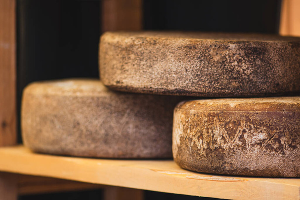 Wheels of homemade bio natural seasoned cheese on wooden shelves, close up - Photo, Image