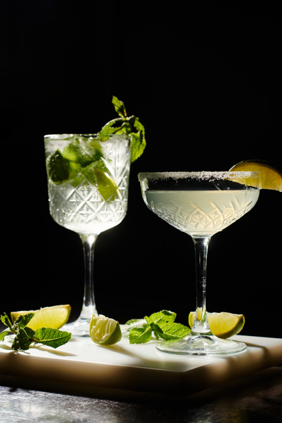 kaksi esteettistä cocktailia koristeltu minttu ja lime viipaleita musta tausta, käsite - Valokuva, kuva