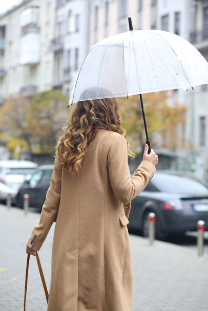 Uma rapariga de casaco bege com um guarda-chuva transparente a descer a rua. A Europa. Viaja. outono friamente. Previsão meteorológica. - Foto, Imagem