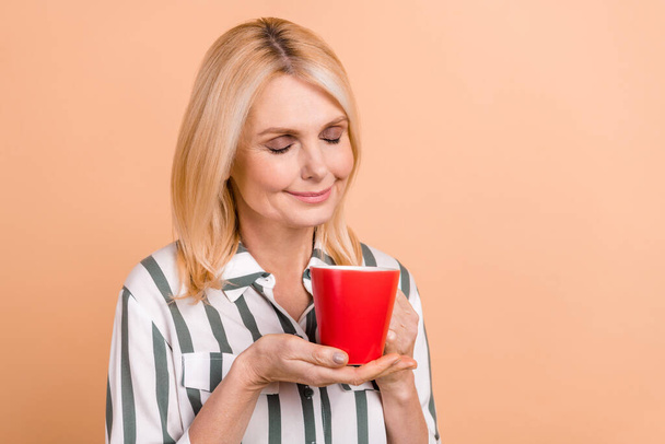 Photo of optimistic senior woman with bob hairstyle striped shirt holding cup enjoy smell of coffee isolated on pastel color background. - 写真・画像