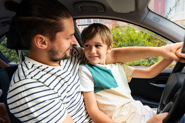 Padre enseñando a su hijo pequeño a conducir en su regazo, mirándose el uno al otro - Foto, imagen