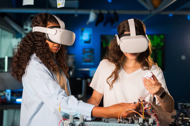 Two young women in VR glasses doing experiments in robotics in a laboratory. Robot on the table - Photo, Image