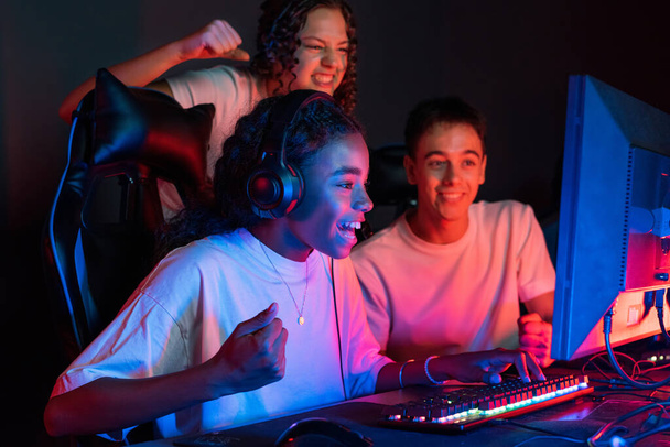 Video oyunu kulübünde mavi ve kırmızı ışıklı video oyunları oynayan çok ırklı bir grup genç. Zafer için heyecanlandım. - Fotoğraf, Görsel