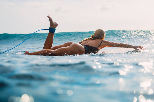 Surfer woman in sexy bikini rowing on surfboard. Active water sport and summer vacation - Photo, Image