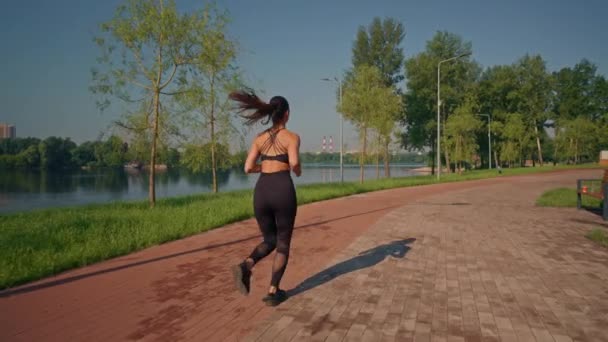 peruutusnäkymä nainen kulkee pitkin jokea kesäpuistossa aerobinen liikunta aamulla hidastettuna - Materiaali, video