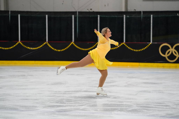 Mosinee, Wisconsin USA - 26 lutego 2021: Młoda dorosła kobieta w pięknej żółtej sukience brała udział w zawodach łyżwiarskich w stanie borsuk zima - Zdjęcie, obraz