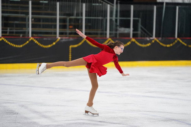 Mosinee, Wisconsin USA - 26 lutego 2021: Młoda dorosła kobieta w pięknej czerwonej sukience brała udział w zimowych igrzyskach borsuka na łyżwach. - Zdjęcie, obraz